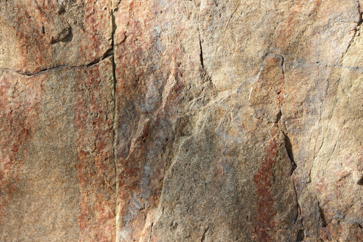 Close-up of natural stone texture with subtle mineral variations and surface cracks, earth-based.